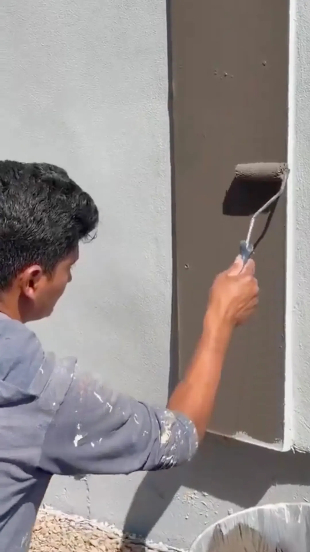 Painter rolling Sherwin-Williams Urbane Bronze SW 7048 onto a trim band over light blue-gray Krypton stucco